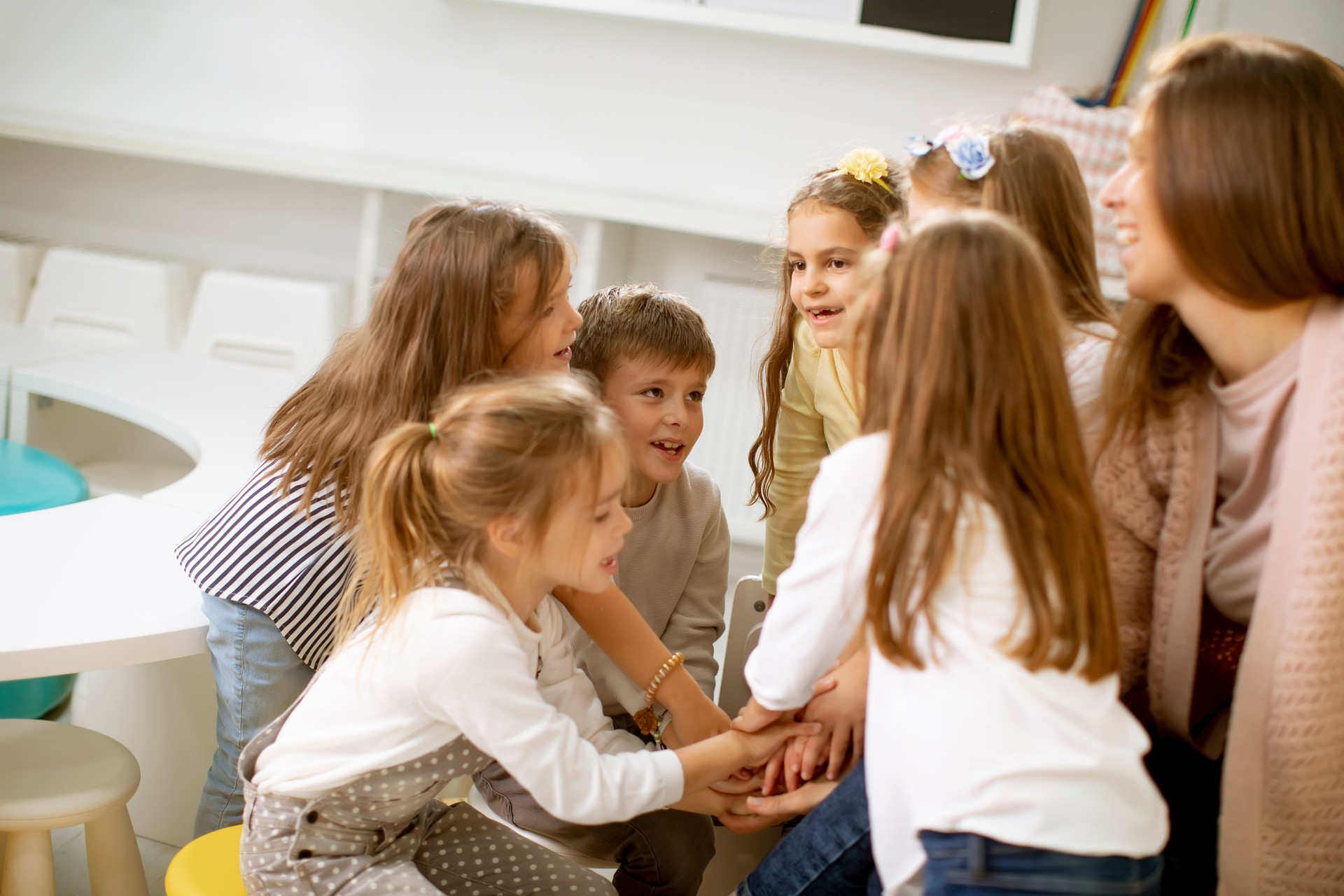 Cute preschool kids put hands together with their nursery teacher